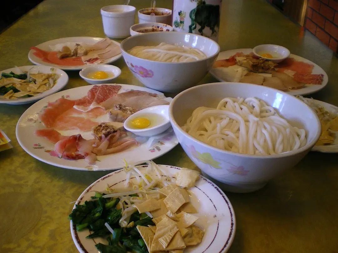 Plates of raw sliced meat, eggs, tofu skin and rice noodles set out to add to the broth
