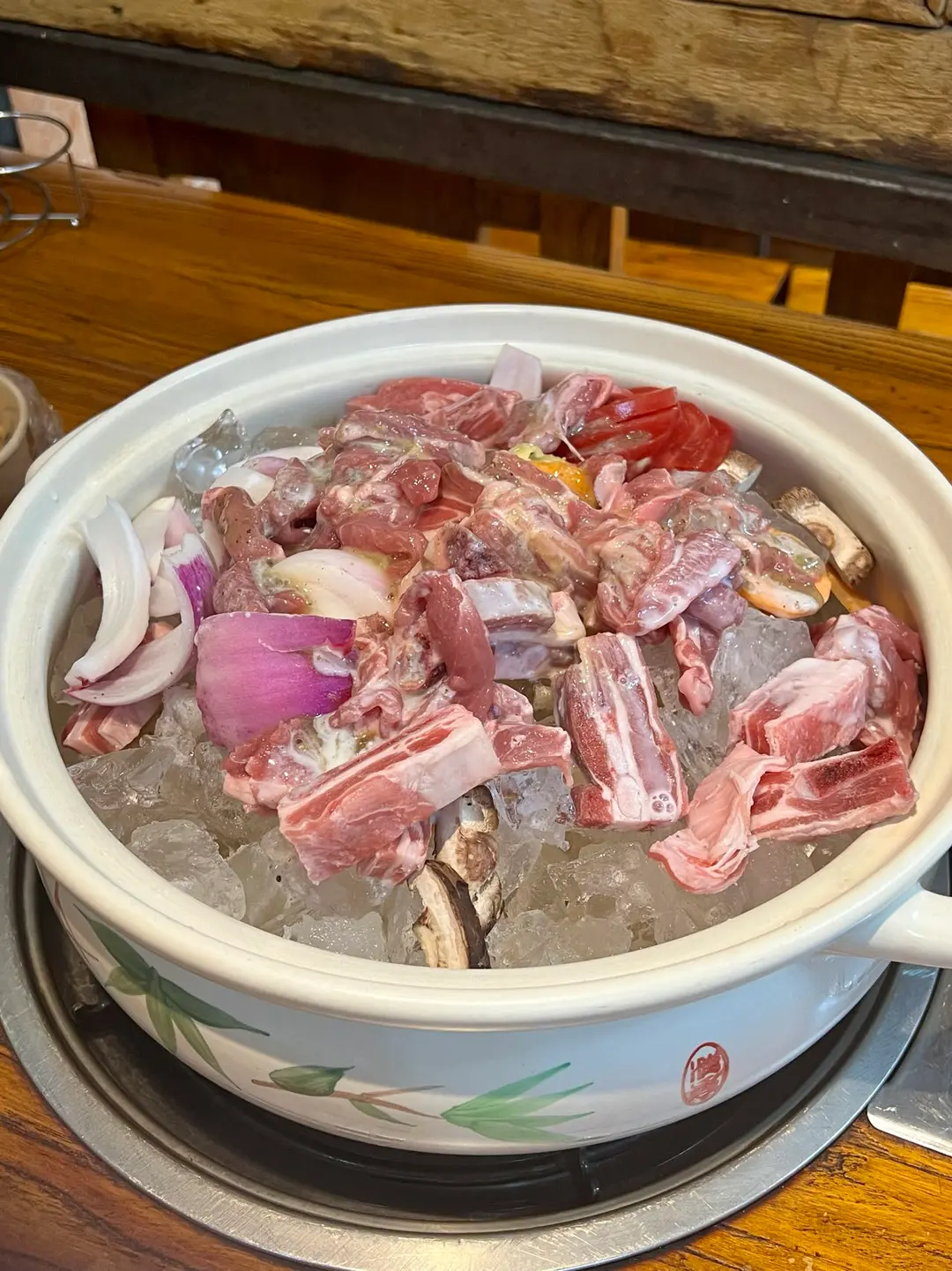 Raw lamb ribs, onion and mushrooms piled on ice cubes in a white pot before cooking