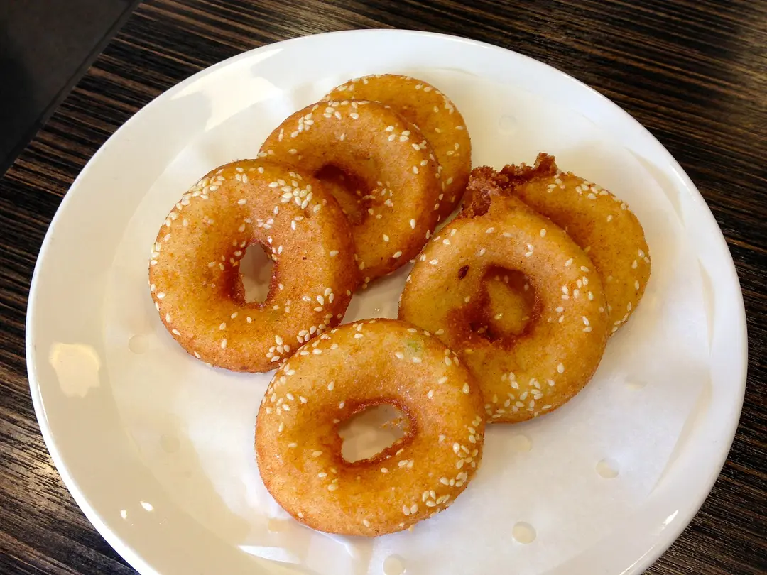 Five golden fried mianwo rings sprinkled with sesame seeds on a white plate