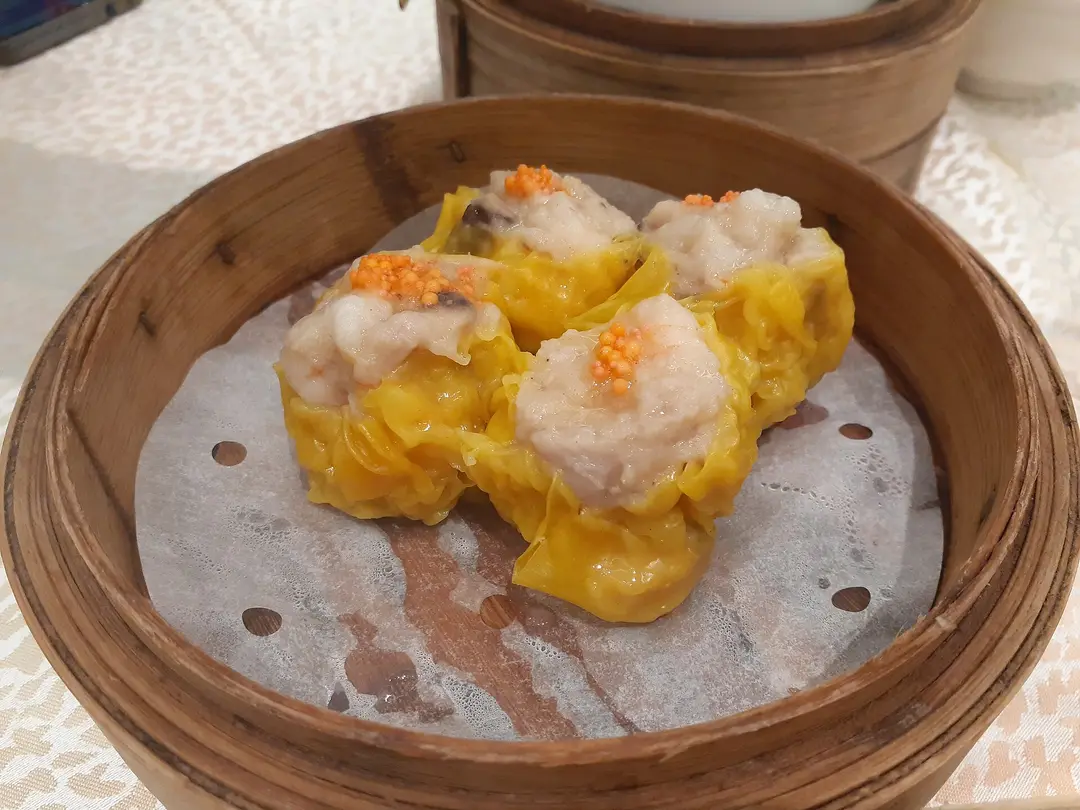 Four siu mai dumplings topped with orange roe in a bamboo steamer