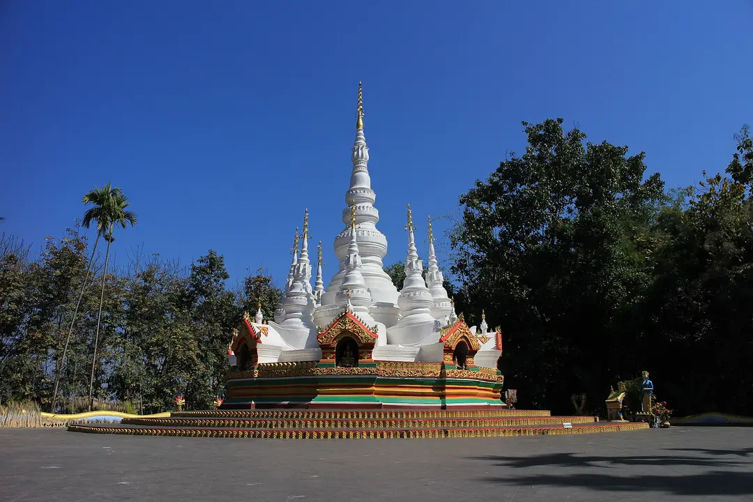 The white, many-spired Manfeilong Pagoda, a Dai Buddhist stupa, under a clear blue sky
