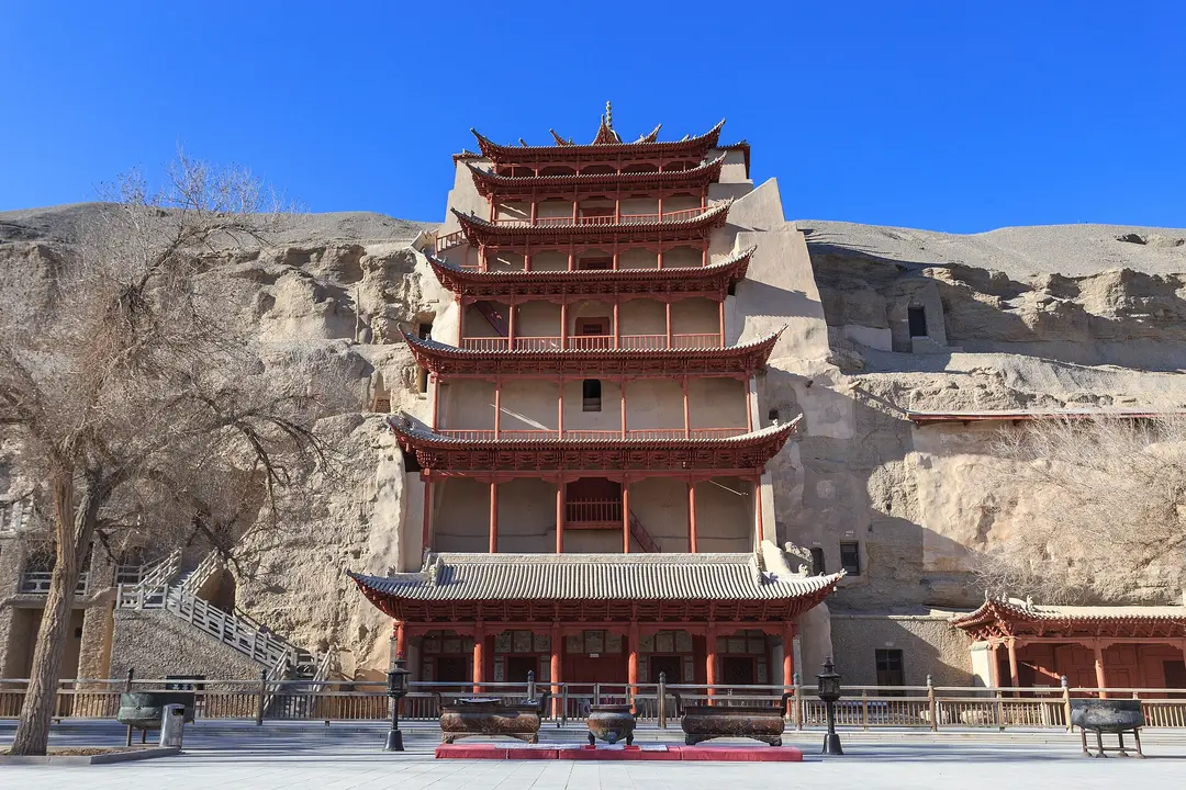 The red nine-storey wooden facade built against the cliff at the Mogao Caves, with bare winter trees