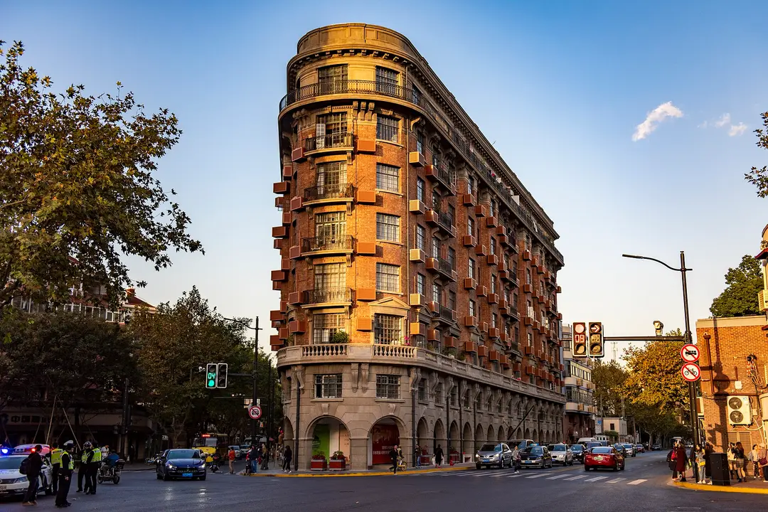 The narrow, ship-shaped end of red-brick Wukang Mansion at a road junction in late afternoon light