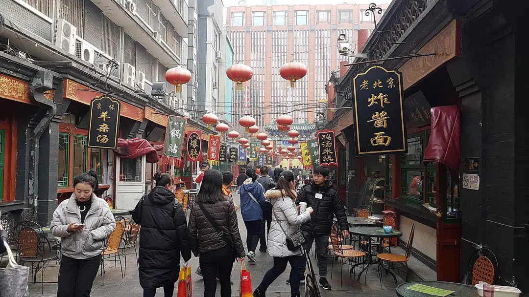 Winter crowds walking down a narrow snack street with red lanterns and old-style shop signs