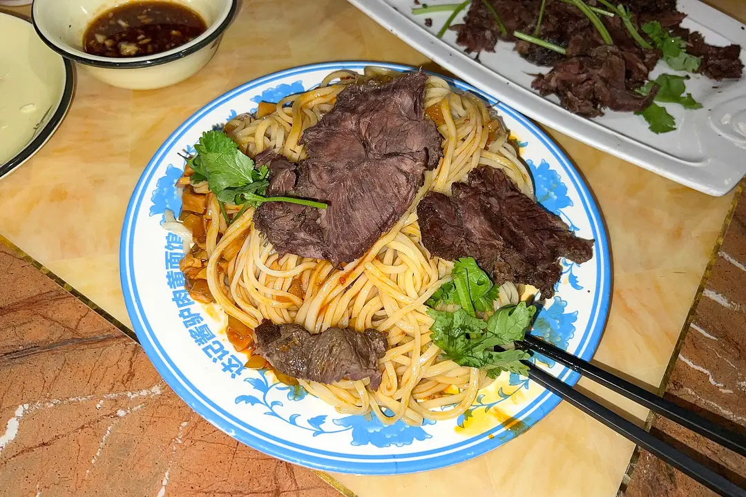 A plate of yellow noodles topped with slices of braised donkey meat and coriander in a Dunhuang restaurant