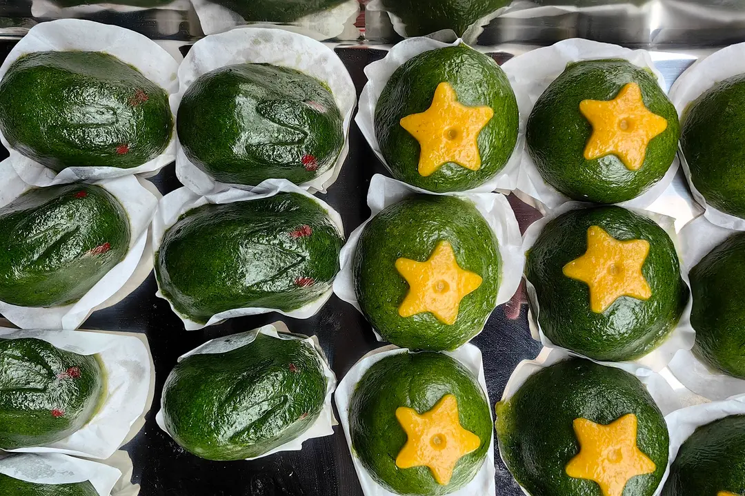 Rows of green qingtuan rice dumplings in paper cups, some topped with a yellow star