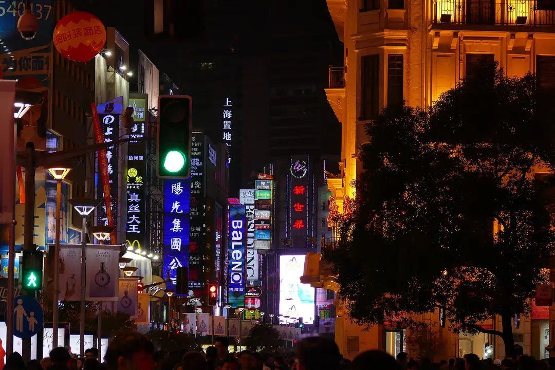 Crowds walking under neon shop signs and a green traffic light on Nanjing Road pedestrian street, Shanghai, at night