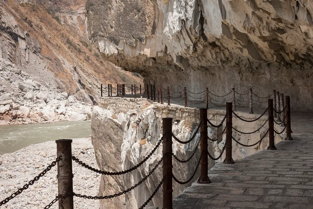 A chain-railed walkway cut into the cliff above the river in Tiger Leaping Gorge