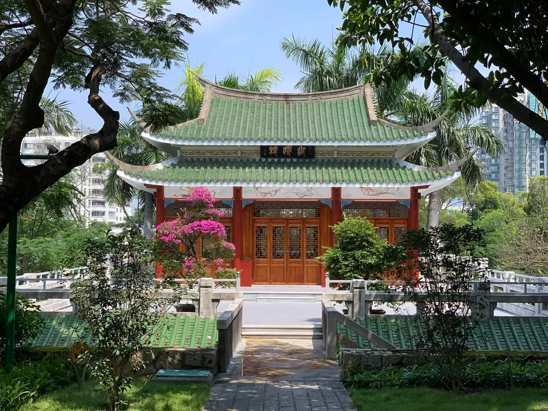 A green-tiled hall with red doors framed by palms and trees at Nanputuo Temple, Xiamen