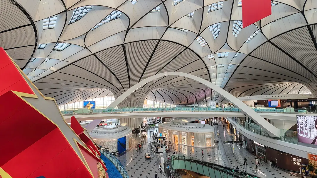 Passengers walking under the curved white roof and arched walkway of Beijing Daxing airport's terminal