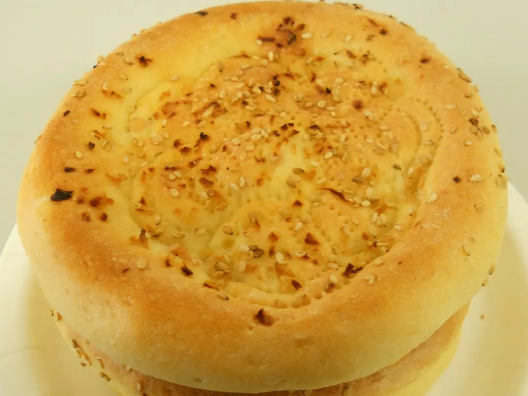 A thick round naan with a raised rim, a stamped center and toasted sesame seeds