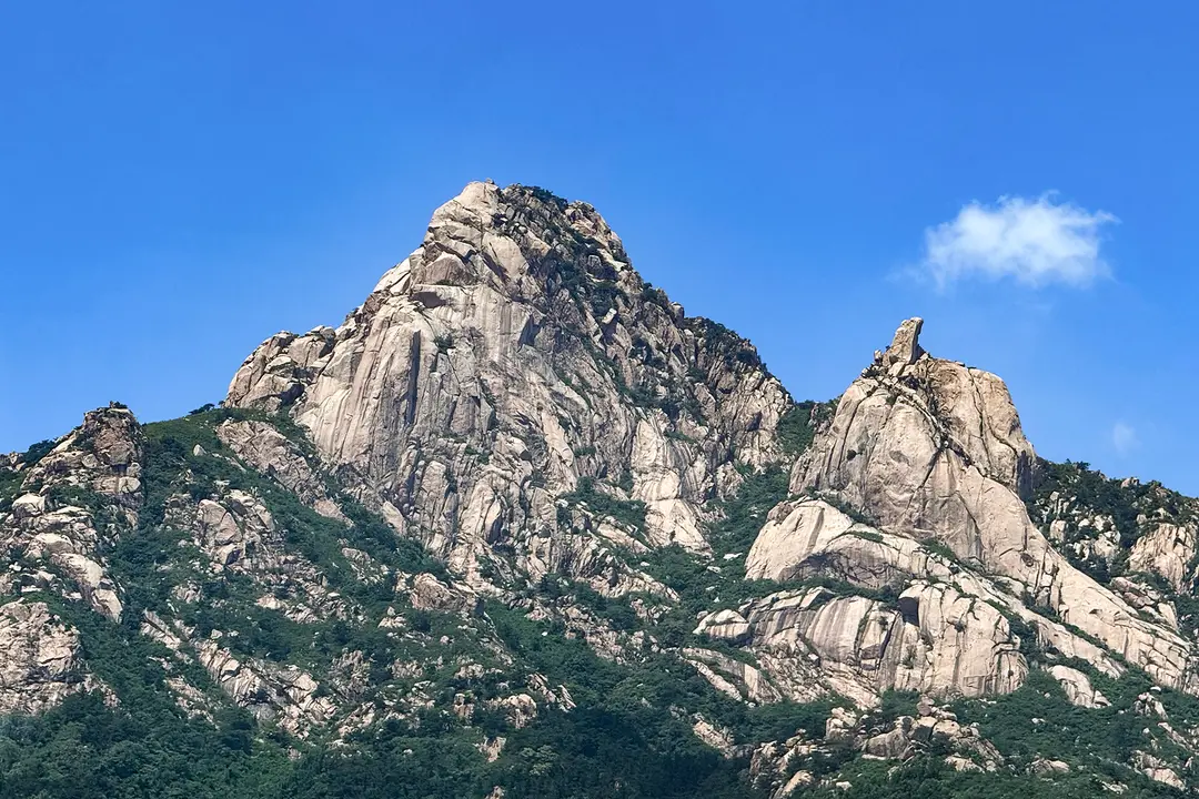 Bare granite peaks rising above green forested slopes on Mount Lao under a blue sky