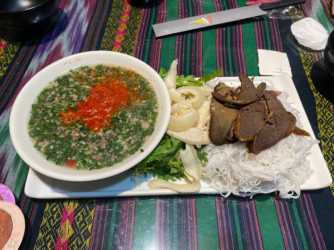 A bowl of green herb dipping sauce beside a plate of sliced beef, rice noodles and onion