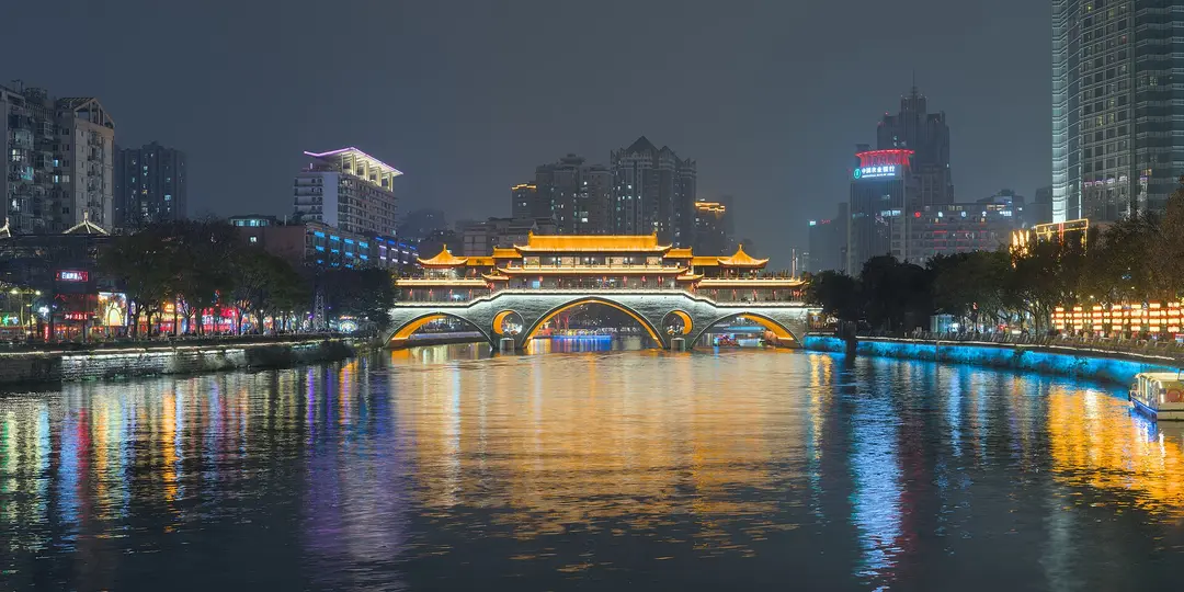 Anshun Bridge lit up at night over the Jin River in Chengdu, with tower blocks behind