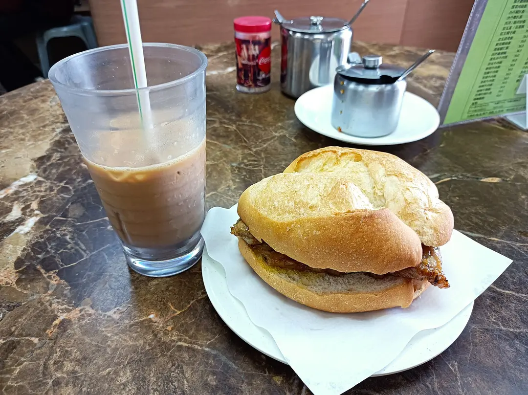 A pork chop in a crusty bun on a plate, beside a glass of iced milk tea