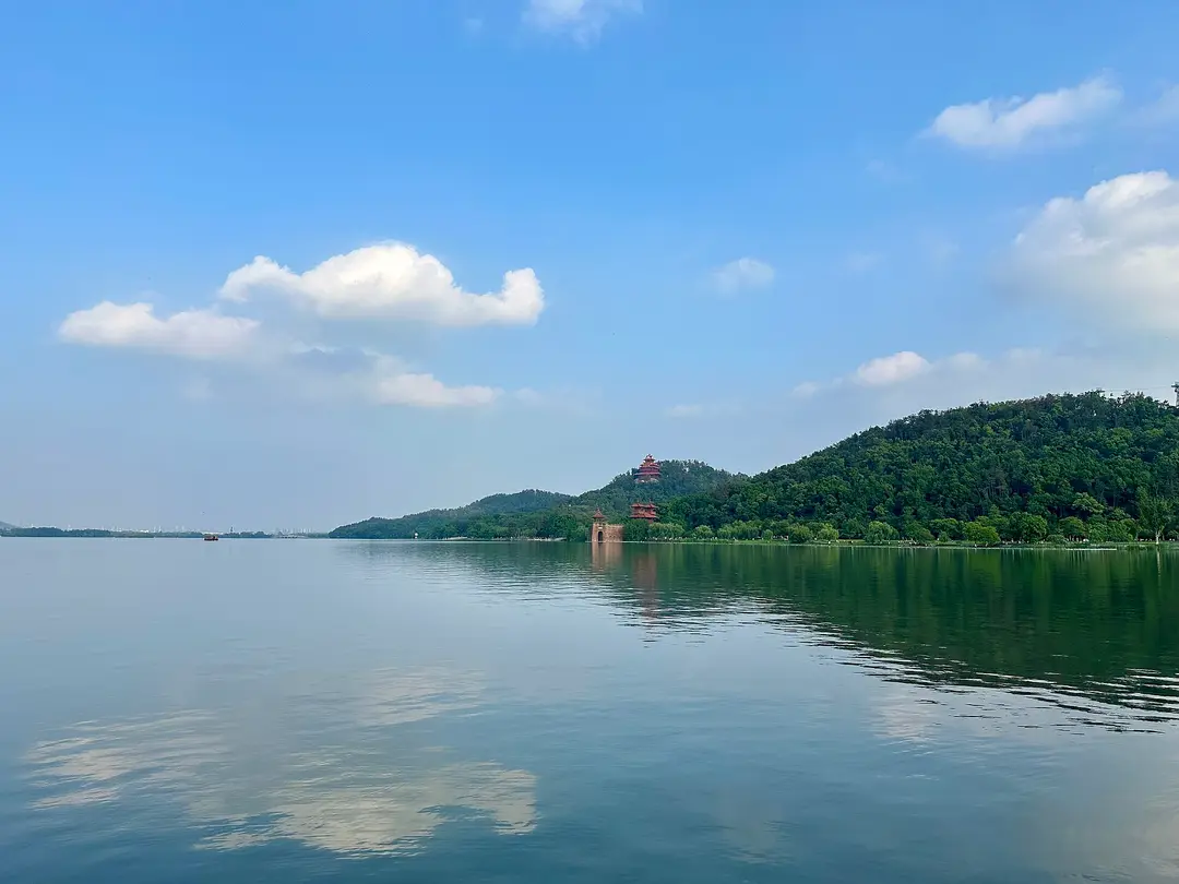 Calm water of East Lake reflecting clouds, with the wooded Moshan hill on the far shore