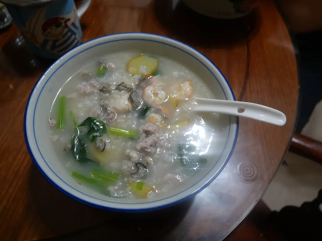 A bowl of rice congee with shrimp, clams and green vegetables