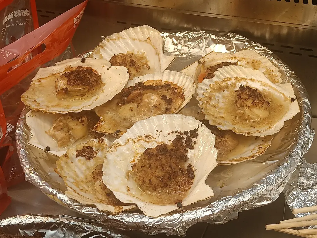 Scallops in their shells topped with browned garlic, on a foil tray