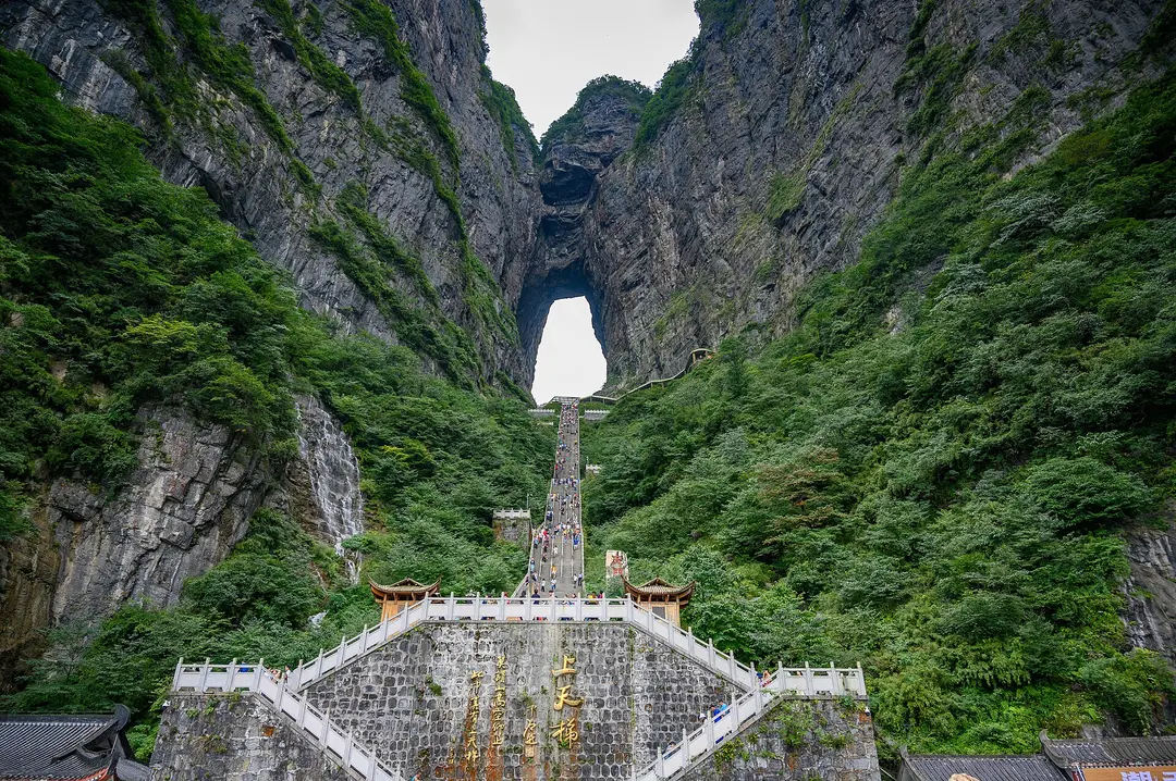 A long stone stairway climbing a green gorge to the natural arch of Tianmen Cave