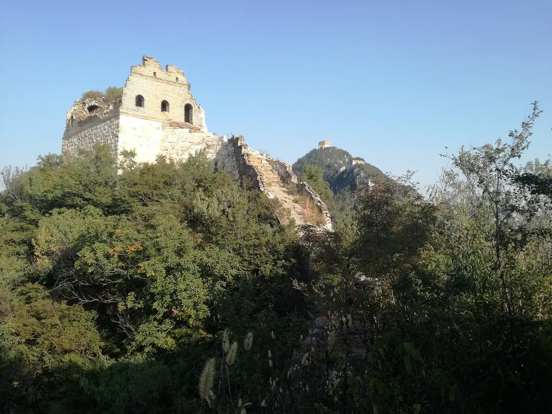A ruined watchtower and crumbling, overgrown wall at Jiankou under a clear blue sky
