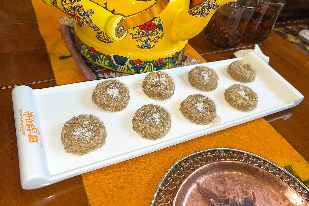 Eight round tsampa cakes in a row on a white tray beside a yellow teapot