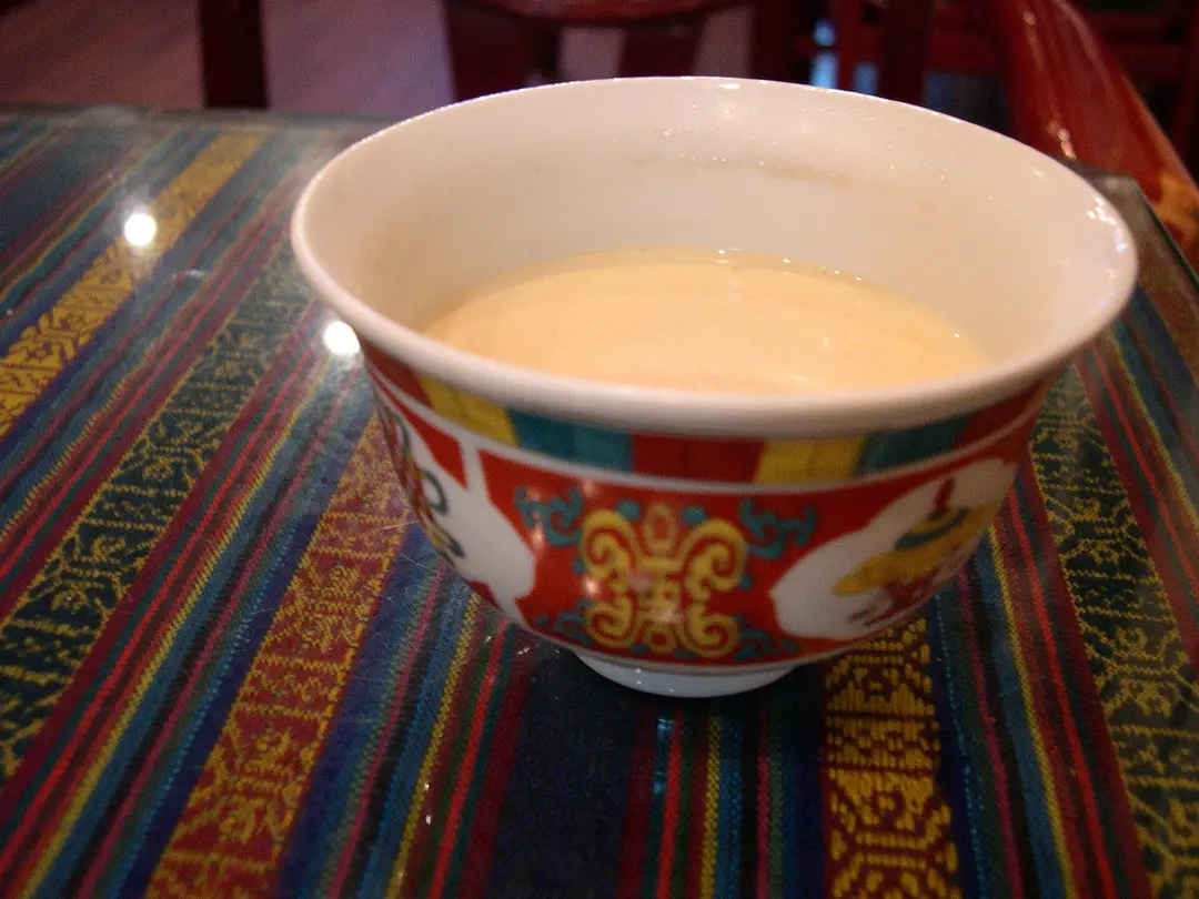 A painted Tibetan bowl of creamy butter tea on a striped woven tablecloth