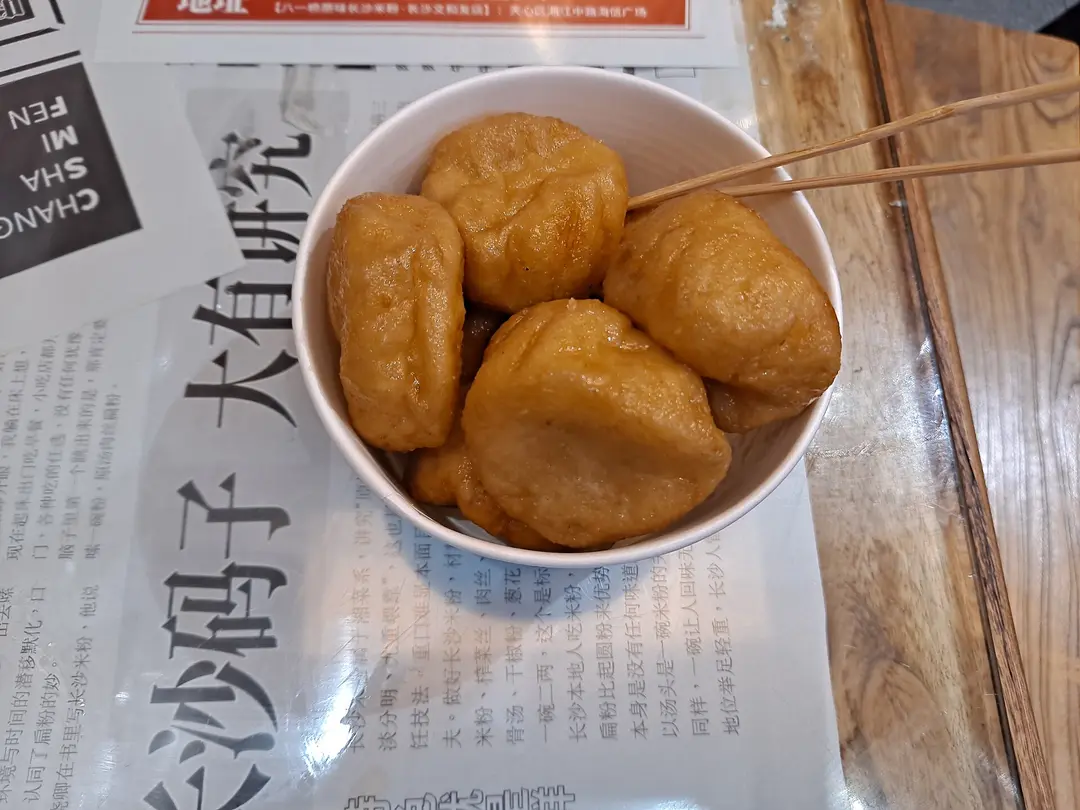 Golden fried glutinous rice cakes in a white bowl with bamboo skewers