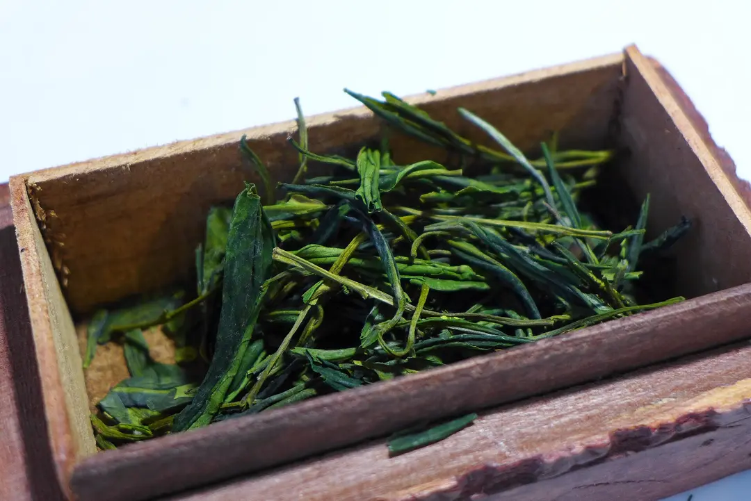 Dry Huangshan Maofeng green tea leaves in a small wooden box
