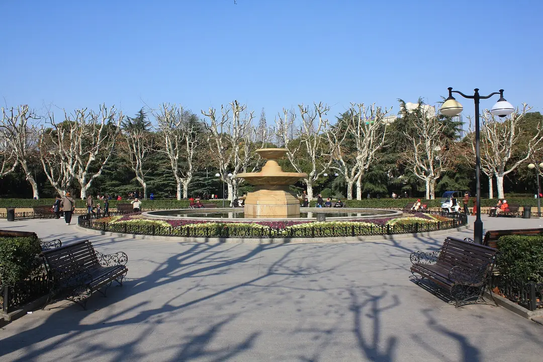 A stone fountain and benches among bare plane trees in Fuxing Park in winter