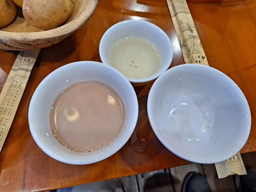 A small bowl of pale barley wine beside a bowl of butter tea at a restaurant in Jiuzhaigou County
