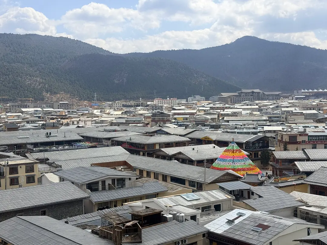 Grey tiled roofs of Dukezong Old Town below forested hills, seen from Guishan Park