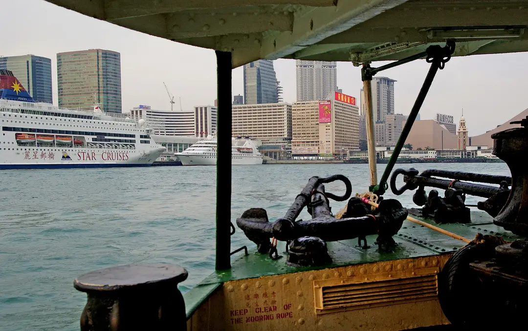 The open bow of a Star Ferry crossing the harbor toward the Tsim Sha Tsui waterfront and its clock tower