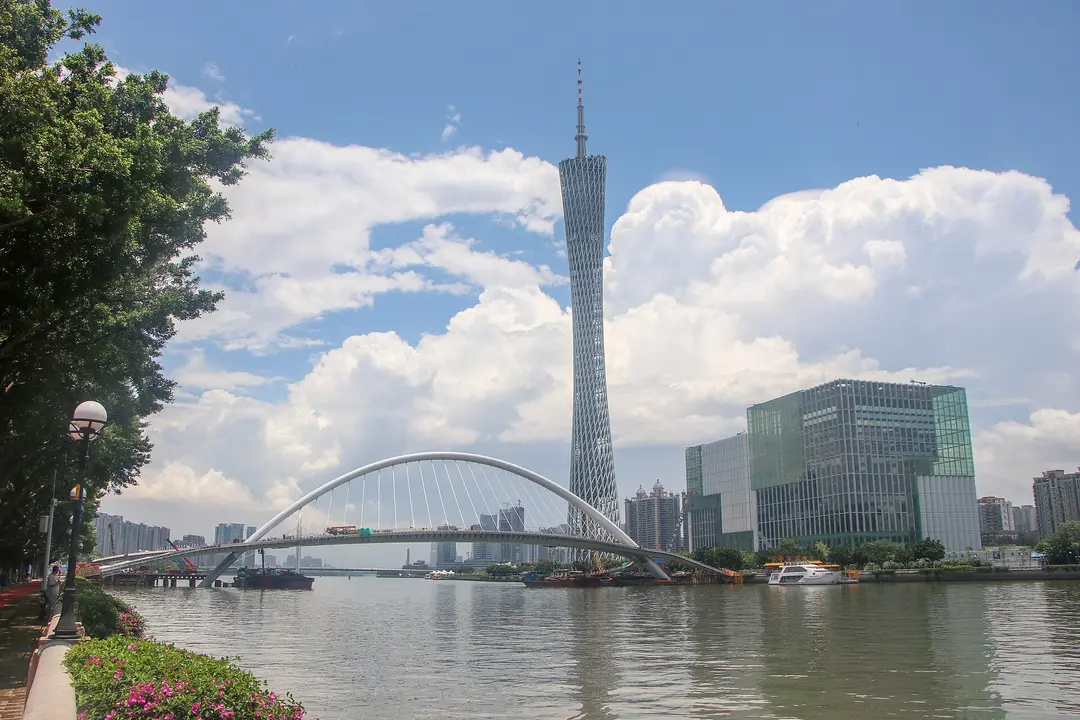 Canton Tower rising behind an arched footbridge over the Pearl River under a cloudy blue sky