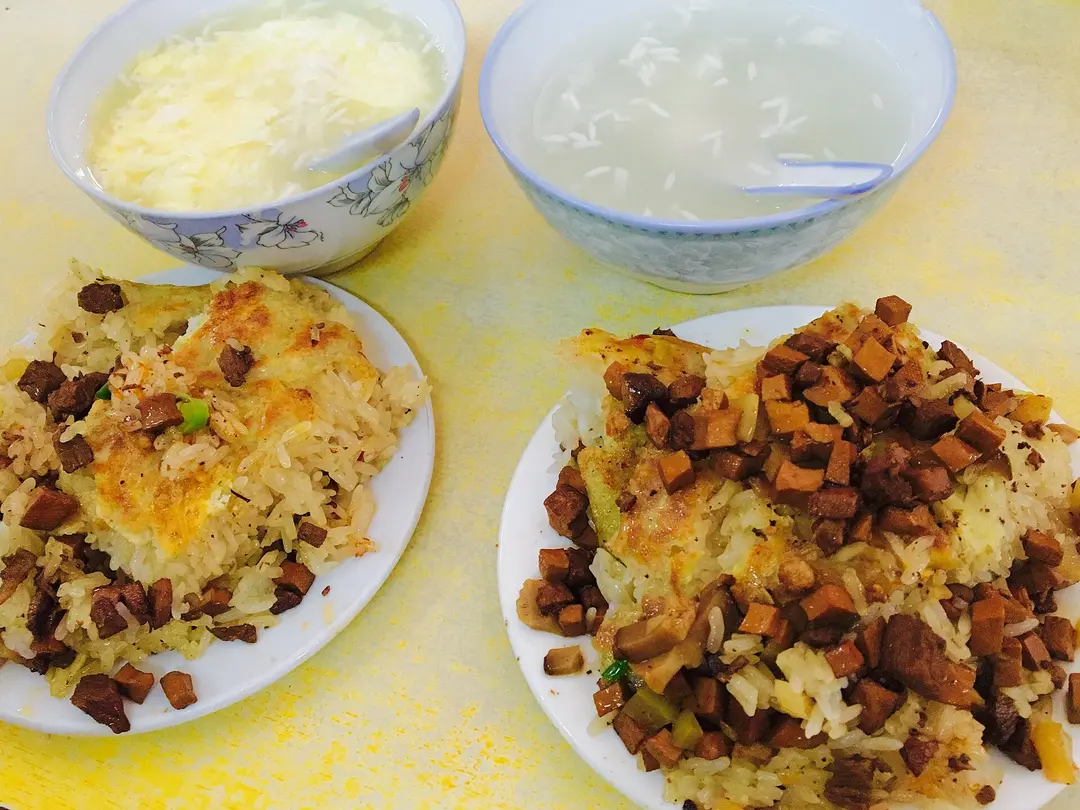 Two plates of doupi, glutinous rice under a golden crust with diced meat, beside bowls of soup