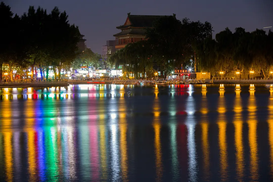 Lights of lakeside bars reflected in Shichahai at night, with the Drum Tower behind the trees