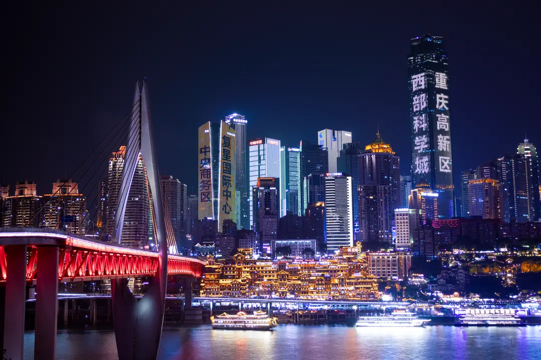 Hongyadong lit gold below Chongqing's towers at night, with Qiansimen Bridge and river boats