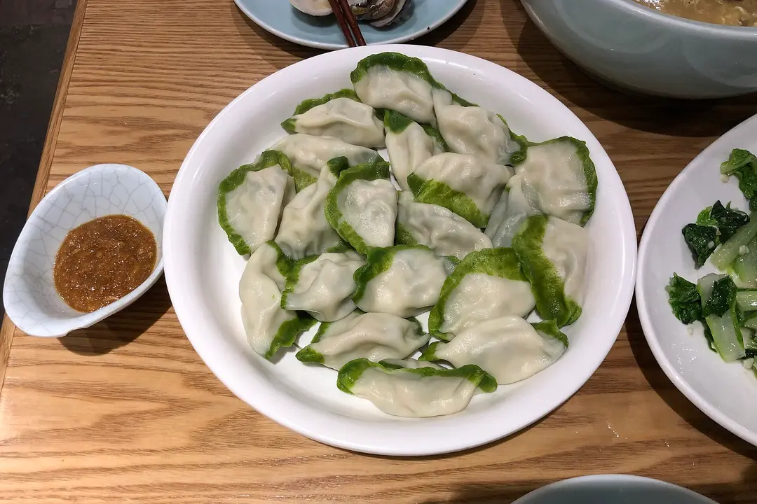Plate of boiled dumplings with green-edged wrappers and a dipping sauce
