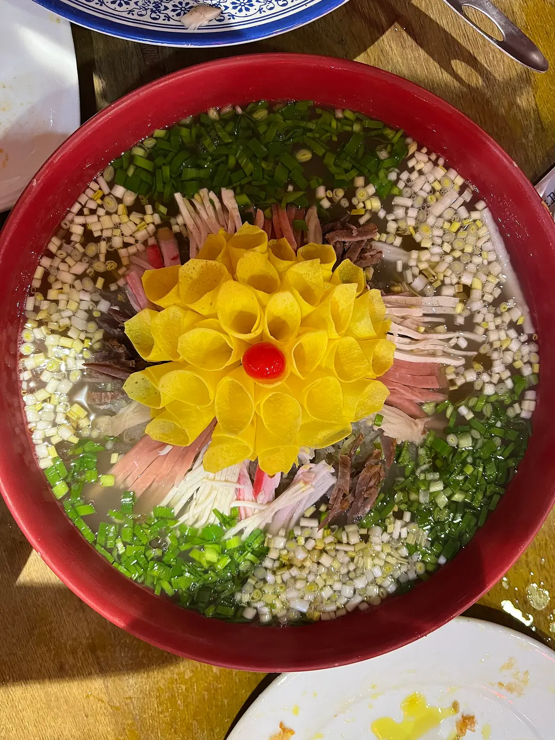 A wide bowl of clear broth with shredded radish, meat and spring onion around a yellow peony