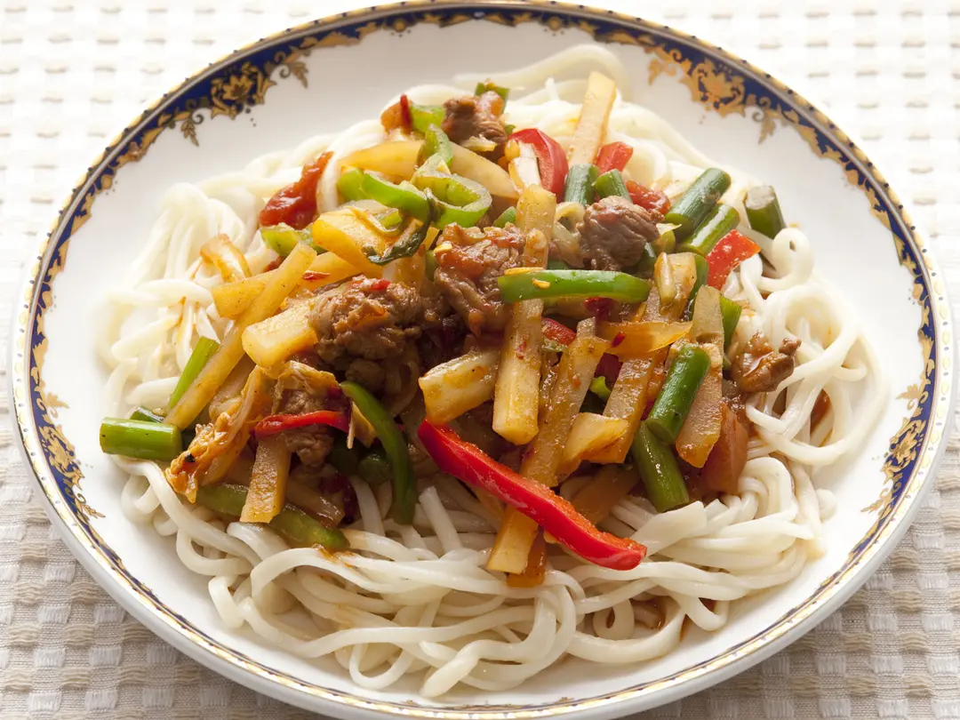 Thick white hand-pulled noodles under stir-fried lamb, red pepper, green beans and potato