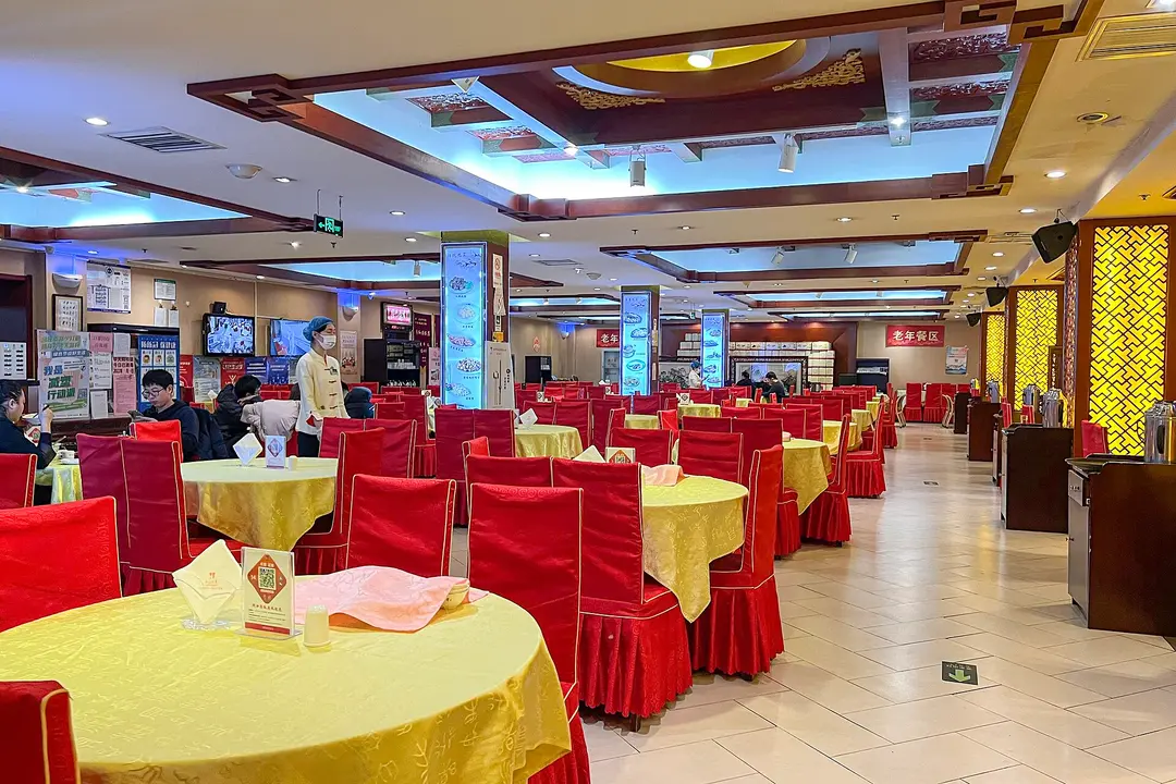 Round tables with yellow cloths, red chairs and a QR payment stand in a Beijing restaurant