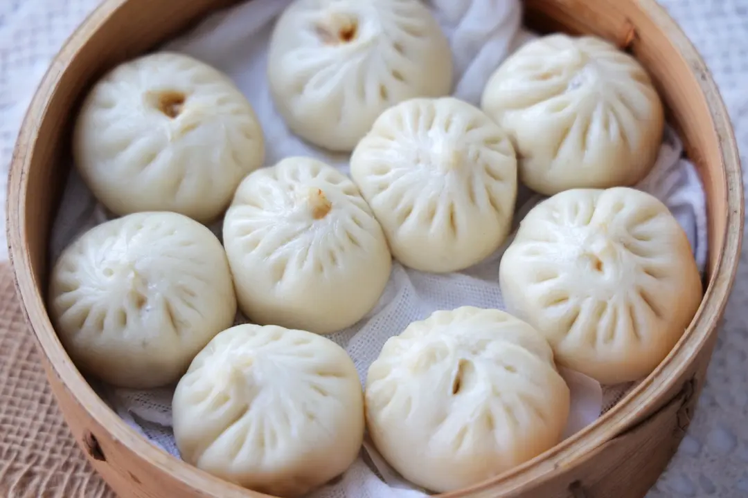 A bamboo steamer of pleated xiaolongbao soup dumplings seen from above