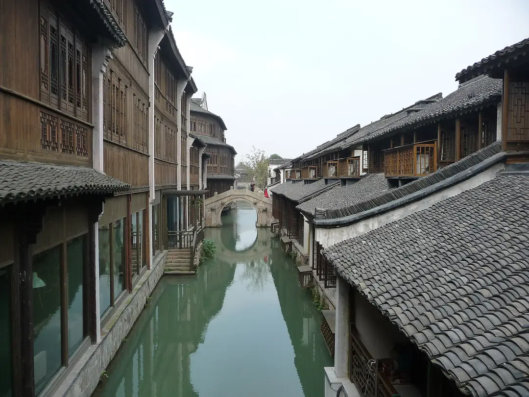 A narrow canal between two-storey wooden houses, leading to an arched stone bridge in Wuzhen