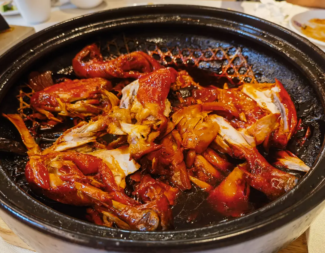 Glossy red-brown pieces of Caocao chicken in a dark clay pot