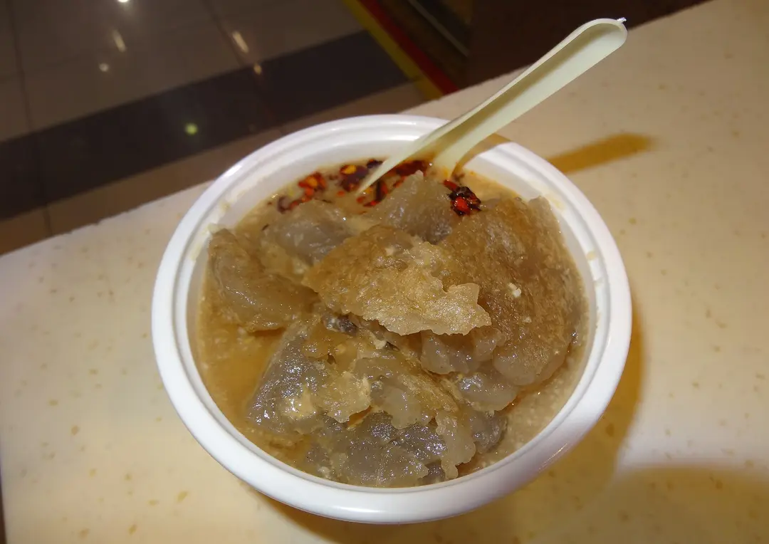 Bowl of translucent fried starch jelly in sesame sauce with chili flakes