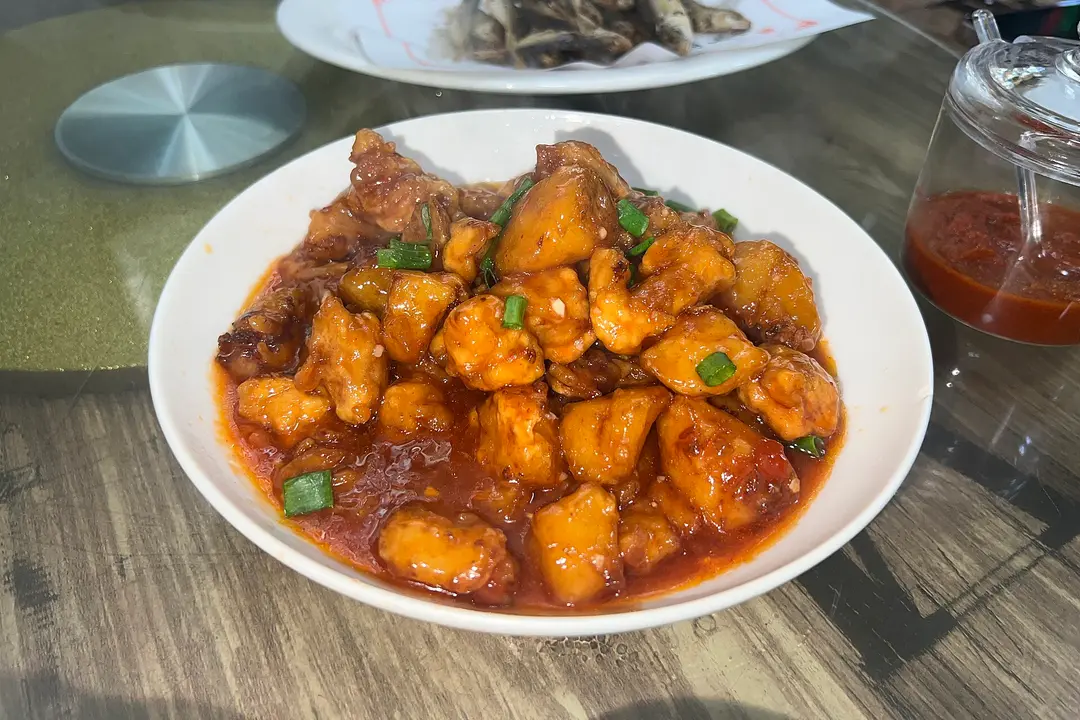 A bowl of lychee pork in glossy red sweet-and-sour sauce with green scallion pieces