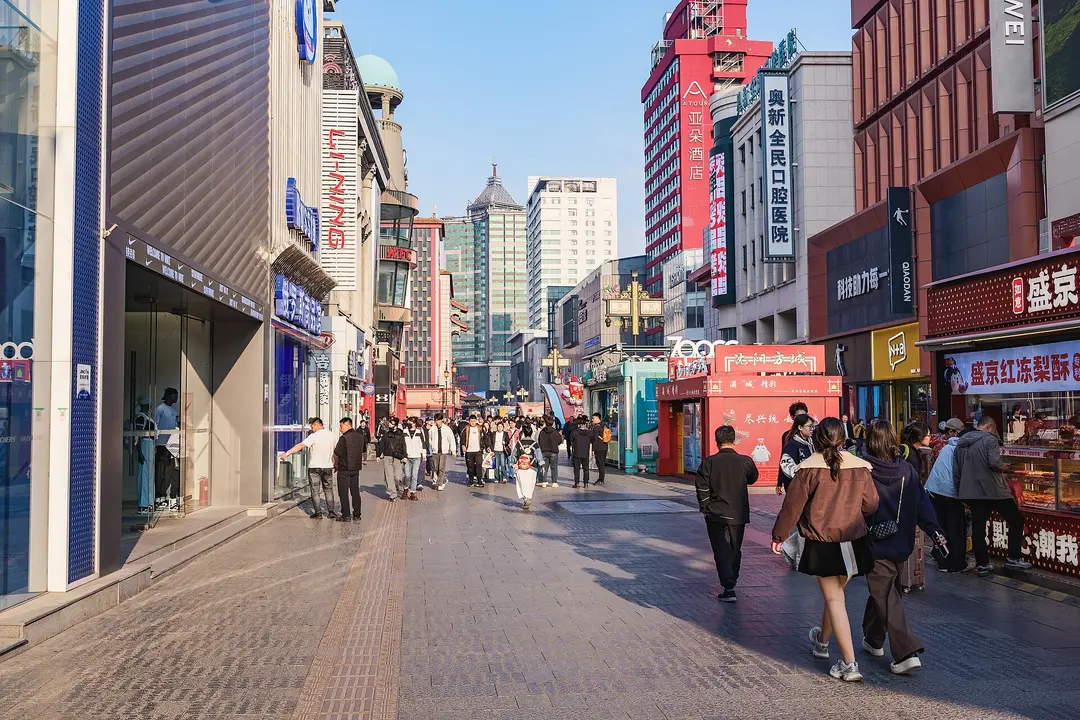 Shoppers walking down the paved Zhongjie pedestrian street between shops and tall signs in spring
