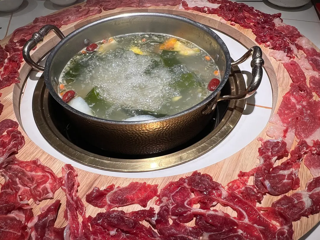 A pot of clear broth ringed by raw sliced beef at a hotpot table