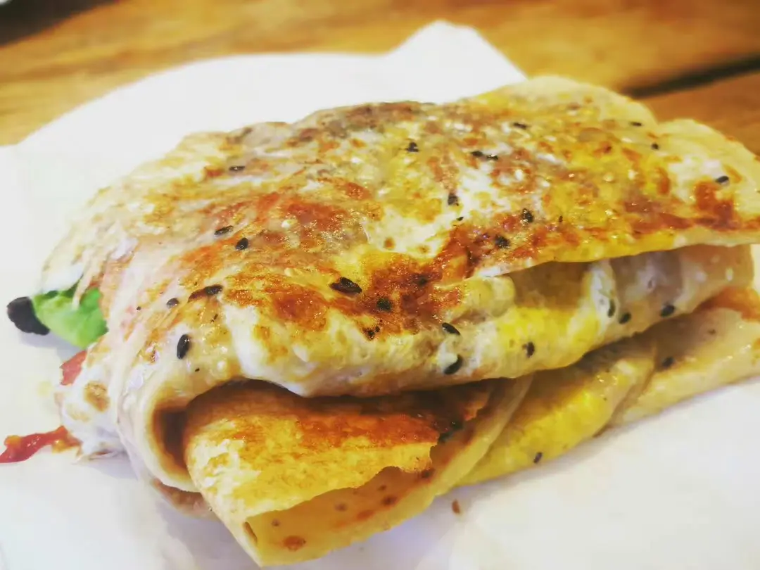 Folded crêpe with egg and sesame wrapped around a filling, on paper