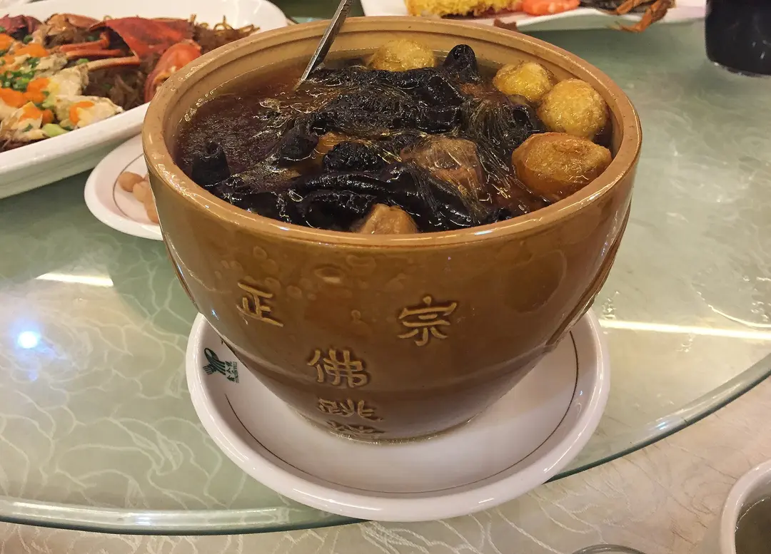 A brown clay jar of Buddha Jumps Over the Wall filled with dark broth, mushrooms and quail eggs