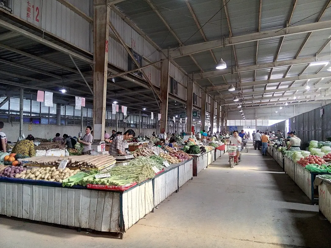 Vendors at vegetable stalls with handwritten Chinese price cards in a covered market in Beijing